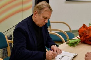 Na zdjęciu autor wpisuje dedykację do książki.